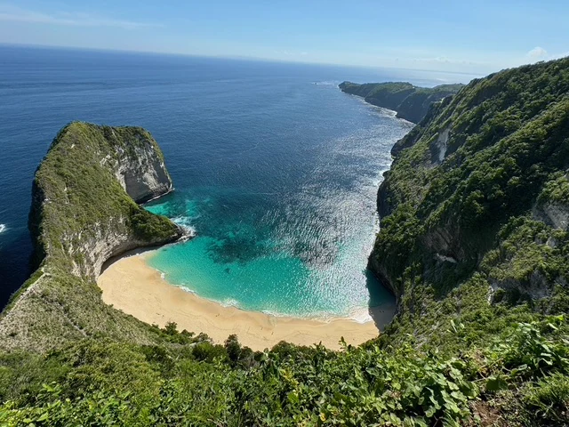 A sheltered turquoise bay and sandy beach framed by steep green cliffs
