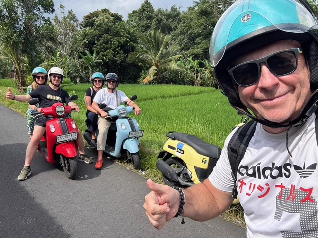 Helmeted travellers with scooters beside a green tropical road
