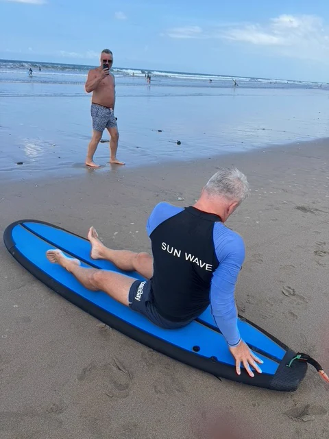 A traveller sitting on a surfboard on a beach beside the sea