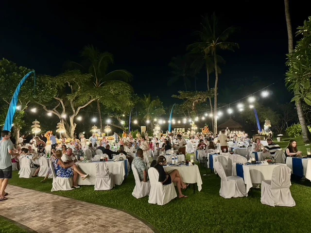 Outdoor dinner tables in a palm-lined garden lit with strings of lights