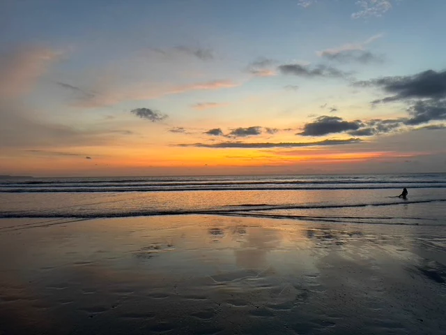 The orange glow of sunset reflected across shallow water on a beach