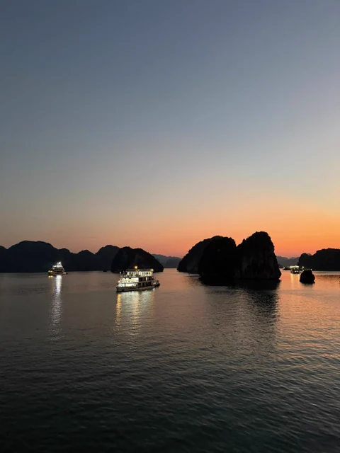 Boats and dark limestone silhouettes against a glowing sunset in Vietnam