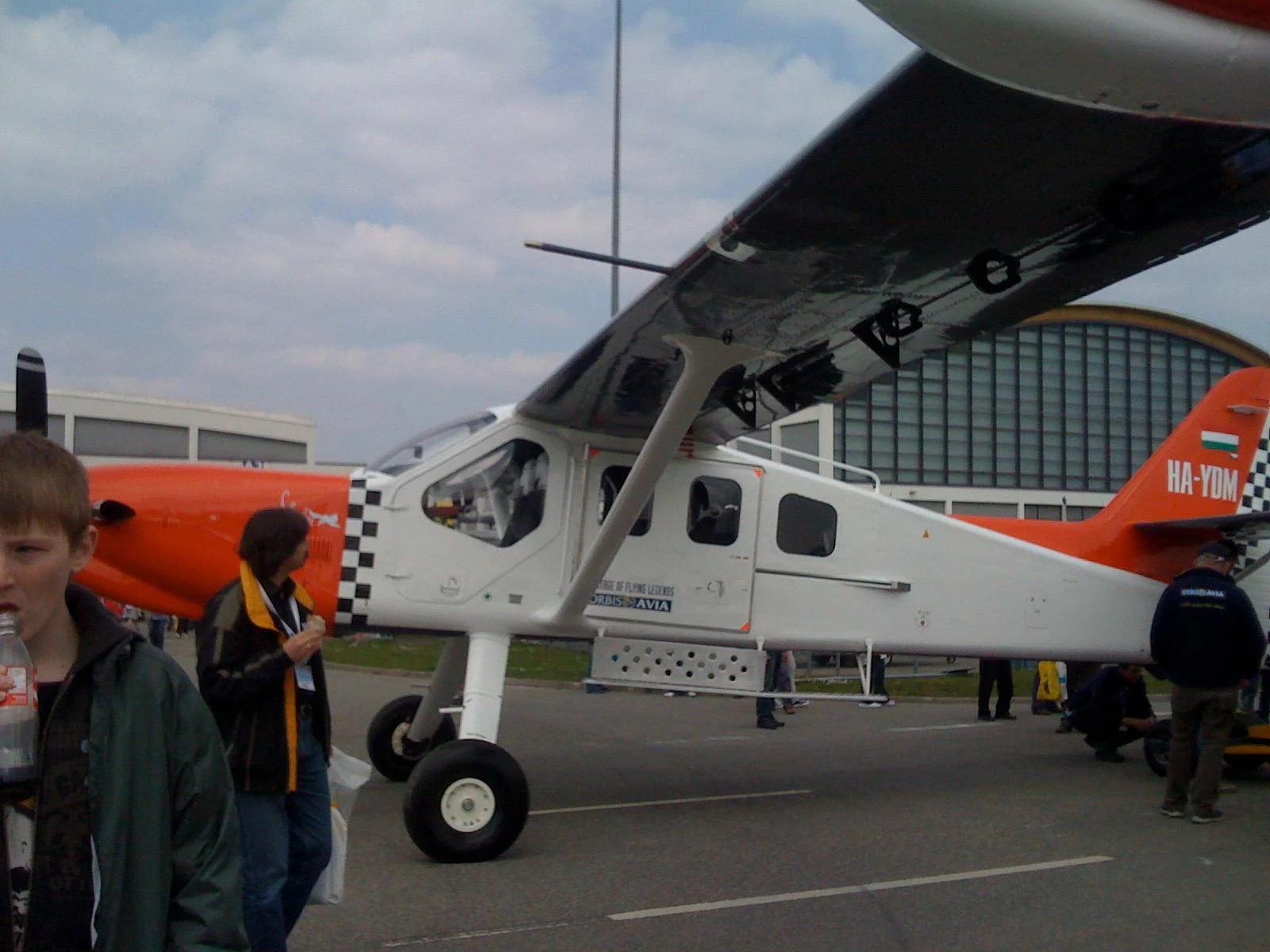 Side view of the white and orange aircraft, with its cabin door open beneath the wing