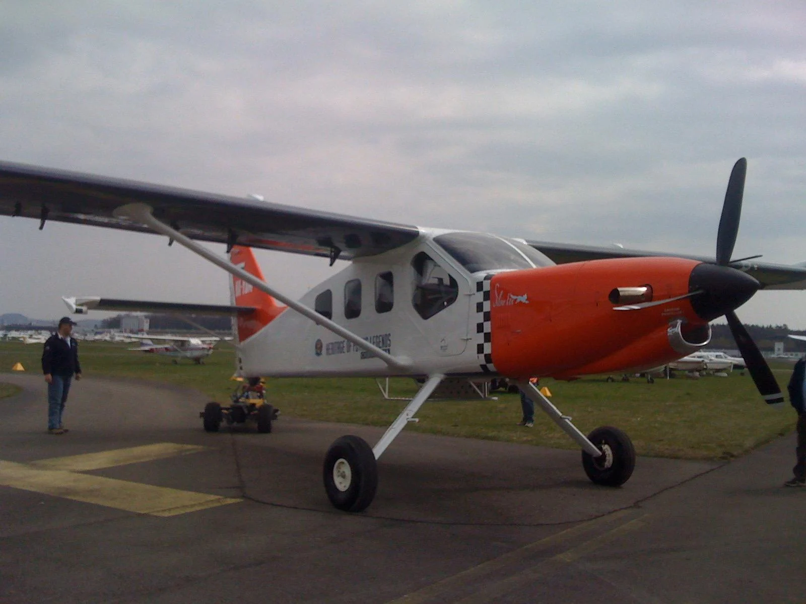 A white and orange high-wing aircraft viewed from the front, with its propeller and landing gear visible